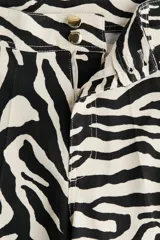 Pantalón de tiro alto confeccionado en lona de algodón con estampado de cebra, corte de perneras rectas y cierre de botones metálicos en la cintura.