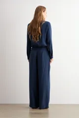 Pantalón de corte recto y tiro medio, confeccionado en tejido negro de textura sutil. Presenta un diseño minimalista con cierre frontal oculto y caída fluida.
