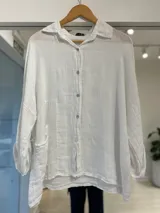Camisa oversize de lino blanca con cuello camisero, cierre frontal de botones y un bolsillo aplicado en el frente. Mangas largas holgadas.