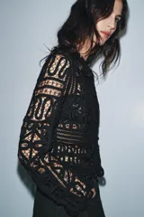 Blusa negra de manga larga confeccionada en tejido tipo crochet con intrincados patrones geométricos y florales. Presenta cuello redondo y cierre frontal con botones.