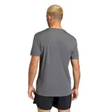 Remera deportiva Adidas de manga corta, color gris, con cuello redondo y logo de la marca estampado en el pecho con un diseño gráfico texturizado.
