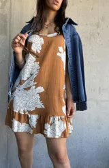 Vestido corto color camel con estampado de flores blancas, sin mangas, con cuello redondo y volados en el ruedo.