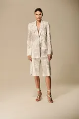 Blazer de sastrería color beige con estampado artístico de motivos orgánicos y trazos suaves. Presenta hombros definidos, solapas de muesca y cierre frontal de un botón.