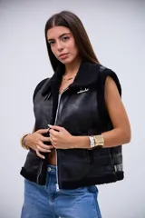 Chaleco de cuero sintético con acabado gamuzado, forrado en corderito negro. Presenta cierre frontal, cuello solapa, detalles de correas ajustables en los laterales y ribetes de corderito en los bordes.