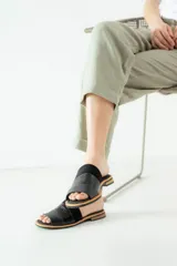 Sandalias tipo chinelas de cuero negro con textura grabada, diseño de banda ancha y suela plana con detalle de borde en color madera.