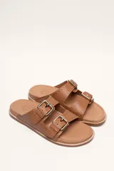 Sandalias de cuero color negro con dos tiras anchas sobre el empeine, cada una con hebillas metálicas ajustables y detalles de tachas plateadas. La suela es de cuero con un borde de color madera.