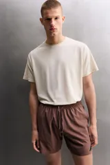 Short deportivo de entrenamiento en color marrón, confeccionado en tejido técnico ligero y elástico. Cuenta con cintura elástica ajustable con cordón, bolsillos frontales, bolsillo trasero con cierre y aberturas laterales en el bajo. Incluye un pequeño detalle de logo estampado en la pierna.
