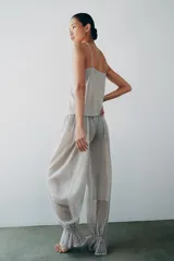 Pantalón abombacho semitransparente de tejido de encaje suave color gris, con tiro medio, cintura elástica y diseño con calados y volantes en los tobillos.
