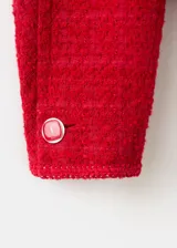 Chaqueta corta roja de tejido texturizado tipo tweed, con cuello redondo, bolsillos frontales con solapa, mangas largas y cierre de botonadura frontal con botones decorativos.