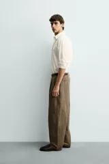 Pantalón de corte relajado confeccionado en mezcla de algodón y lino, con diseño de pliegues frontales, bolsillos laterales y bolsillos traseros de vivo. Presenta cierre frontal con cremallera y botón, con un acabado de lavado especial que le otorga una apariencia única.