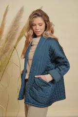 Campera tipo kimono acolchada en color azul petróleo, con diseño de costuras verticales y bolsillos frontales amplios. Presenta mangas largas con puños vueltos y un corte holgado y abierto.