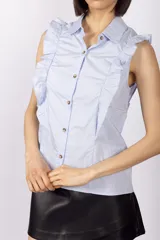 Blusa celeste sin mangas con cuello camisero y volados en los hombros.