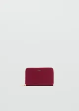 Billetera rectangular de tamaño mediano con cierre perimetral y logo metálico grabado en el frente. Presenta una textura granulada y un diseño compacto.