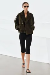 Trench corto de Zara, confeccionado en tejido con algodón con acabado repelente al agua. Presenta cuello solapa, cierre frontal cruzado con botones, mangas largas con trabillas ajustables y bolsillos delanteros.