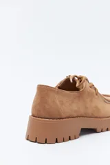 Zapato de gamuza color marrón con cordones, puntera con costura marcada y suela robusta dentada.