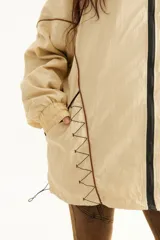 Campera rompevientos beige de nylon con diseño oversize, cuello alto, cierre frontal negro y detalles de costuras y ribetes en contraste.