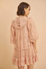 Vestido corto de encaje color durazno, con diseño de volados en capas, mangas largas abullonadas y cuello redondo con detalles bordados.