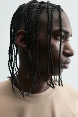 Camiseta de manga corta y cuello redondo, color beige claro, con corte relajado (relaxed fit) y un pequeño texto bordado en el pecho.