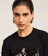 Remera negra de algodón con corte slim, cuello redondo y mangas cortas. Presenta un bloque rectangular frontal con lentejuelas plateadas.