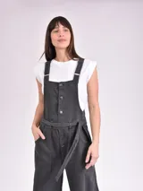 Monoprenda larga de denim gris oscuro, con diseño estilo overall, tirantes ajustables, cierre frontal de botones metálicos y bolsillos frontales grandes. Incluye un cinturón ajustable del mismo material.