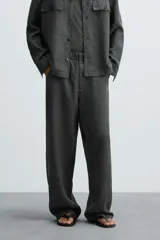 Pantalón de corte relajado confeccionado en tejido de cáñamo color blanco roto. Presenta cintura elástica con cordón interior ajustable, cierre frontal con botones, bolsillos laterales y un bolsillo trasero de plastrón.