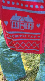 Balaclava tejida con diseño de capucha integrada y bufanda larga, confeccionada en una mezcla de algodón y acrílico con motivos geométricos en tonos rojo y azul.