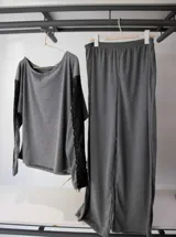 Conjunto de pijama gris compuesto por un buzo de manga larga con escote redondo y detalle de puntilla elastizada en el escote, y un pantalón liso de tiro alto.