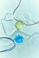 Collar con cordón marrón y dije rectangular de acrílico verde, y collar con cordón azul y dije de acrílico celeste con forma de estrella.