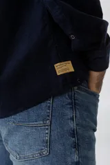 Camisa de pana color azul marino, con mangas largas, cuello clásico y dos bolsillos frontales con solapa y botón.