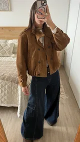 Campera tipo bomber de gamuza color camel, con diseño de doble botonadura frontal, cuello camisero y mangas largas con puños abotonados.