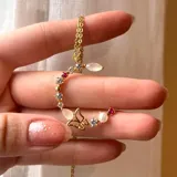 Cadena dorada con dije de letra grande, con piedras y perlas engarzadas.