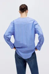 Camisa de algodón con diseño a rayas azules y blancas, corte oversized, escote en V profundo y mangas largas con hombros caídos y puños anchos.