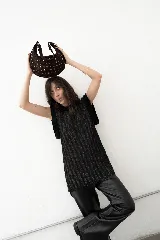 Bolso de mano tipo hobo, confeccionado en gamuza color marrón oscuro, decorado con tachas metálicas circulares en toda su superficie. Cuenta con un asa corta integrada y un diseño curvo distintivo.