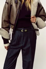 Pantalón de tiro alto y corte tobillero, confeccionado en tejido de aspecto denim oscuro. Presenta diseño de pinzas frontales, bolsillos laterales y cierre frontal con cremallera, botón y gancho. Incluye un cinturón fino a tono con hebilla metálica dorada.