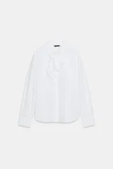 Camisa de popelín blanca con cuello solapa decorado con puntilla y lazo frontal. Presenta mangas largas con puños abotonados y cierre frontal con botones.