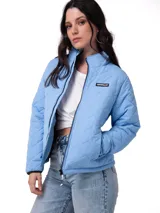 Chaqueta acolchada de color azul claro con diseño de costuras en zigzag. Presenta cierre frontal, cuello alto, bolsillos laterales con cierre y parche con logo de la marca en el pecho.