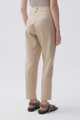 Pantalón chino color beige confeccionado en lino metalizado, de tiro medio-alto y pierna recta. Cuenta con bolsillos laterales y en la espalda.