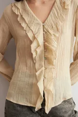 Blusa color beige de manga larga, con escote en V adornado con volados y cierre frontal con botones.