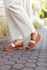 Mocasines de cuero color tostado, con detalle de antifaz en cuero crudo y borlas decorativas. Hechos a mano en Uruguay.