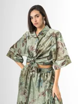 Camisa de organdí verde con estampa floral de inspiración oriental, cuello camisero, mangas cortas amplias y cierre frontal con botones.