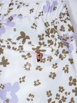 Short de baño blanco con estampado floral en tonos lila y marrón. Cuenta con cintura elástica, cordón ajustable, protección UV50, dos bolsillos laterales, un bolsillo trasero con cierre y suspensor de malla fina hipoalergénica.