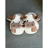 Pantuflas de peluche con diseño de vaca, confeccionadas en piel sintética suave. Cuentan con suela de goma antideslizante y diseño abierto en el talón.