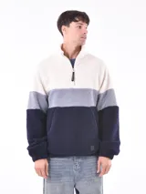 Buzo de tejido polar texturizado, color azul petróleo, con cuello alto y cierre parcial frontal. Presenta un diseño de bloques de color horizontal: blanco crema en la parte superior, gris claro en el medio y azul petróleo en la parte inferior y mangas.