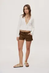 Short de tiro bajo con textura efecto gamuza color beige, bolsillos delanteros y detalle de cordones entrecruzados en la parte frontal.