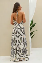 Vestido largo color blanco con estampado de palmeras en tonos negros y dorados, con escote halter y diseño fluido sin mangas.