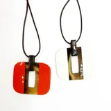 Colgante con dije cuadrado de asta esmaltada color rojo y blanco, con detalle de asta natural en el centro. Cordón encerado negro.