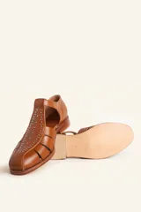 Sandalias de cuero color marrón, tipo romanas, con talón cerrado, tira en T con detalles de tachas metálicas, aberturas laterales y cierre de hebilla ajustable. Tienen tacón bajo de madera.