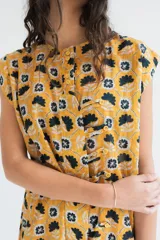 Vestido corto sin mangas en color rosado con estampado floral en blanco y negro. Presenta una cartera de botones asimétrica en el frente y detalle de volado fruncido en el ruedo. Confeccionado en algodón liviano.