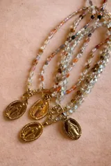 Collar compuesto por una cadena de piedras naturales facetadas en tonos translúcidos, beige y tierra, con un dije central de la Medalla Milagrosa en metal dorado.