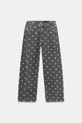 Jeans de tiro medio con corte relajado y largo al tobillo. Presenta un diseño de cinco bolsillos, cierre frontal con cremallera y botón metálico, y un estampado integral de lunares blancos sobre fondo gris oscuro.
